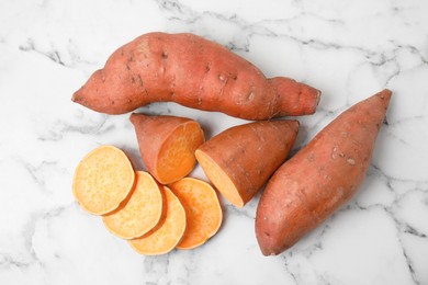 Whole and cut ripe sweet potatoes on white marble table, flat lay