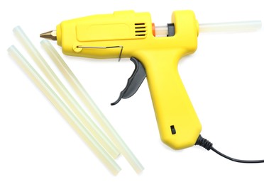 Photo of Yellow glue gun and sticks on white background, top view