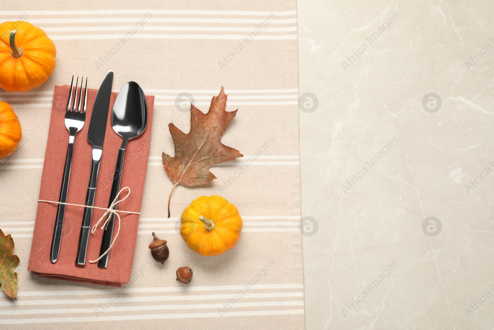 Photo of Cutlery, napkin and autumn decoration on beige marble background, flat lay with space for text. Table setting