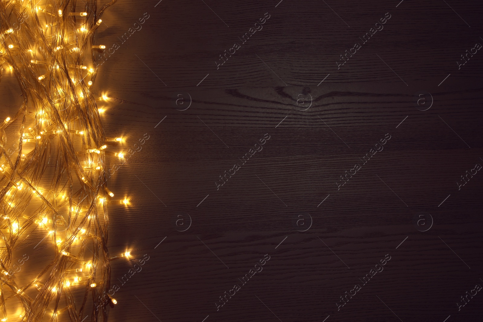 Photo of Beautiful glowing Christmas lights on wooden table, top view. Space for text