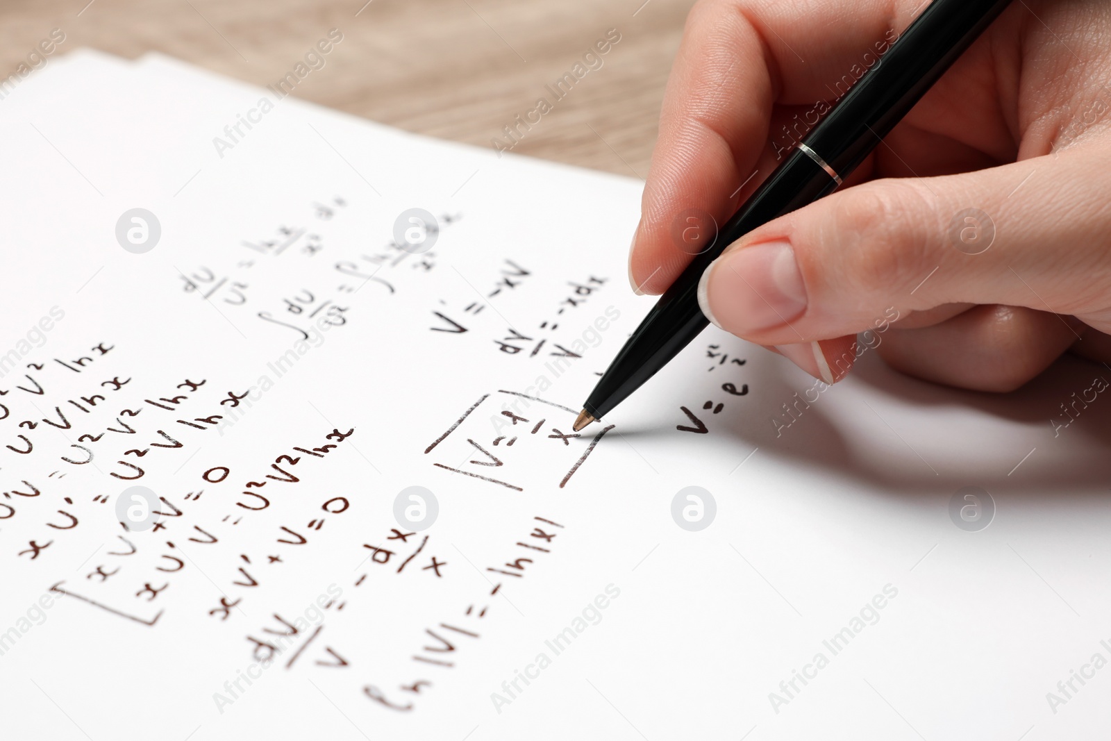 Photo of Student writing different mathematical formulas on paper, closeup