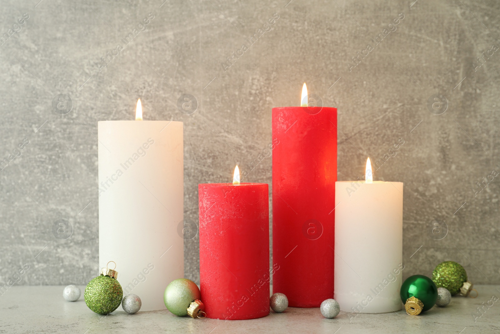 Photo of Burning candles with Christmas baubles on light grey table