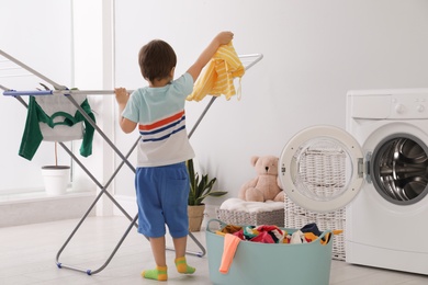 Cute little boy hanging laundry onto clothes drying rack indoors, back view