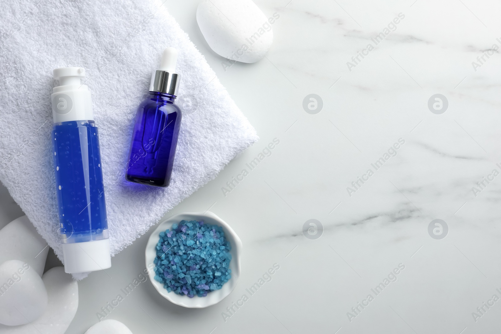 Photo of Spa composition. Bottles of cosmetic products, sea salt, towel and stones on white marble table, top view. Space for text