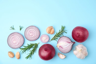 Fresh red onions, garlic and rosemary on light blue background, flat lay. Space for text