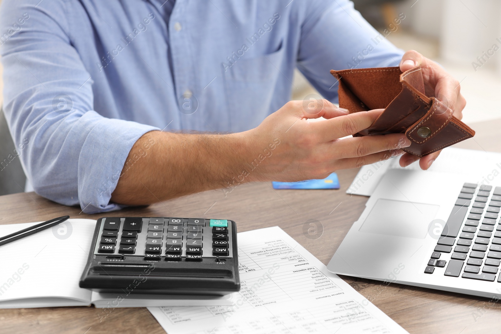 Photo of Man with empty wallet, laptop and calculator planning budget at table indoors, closeup. Debt problem