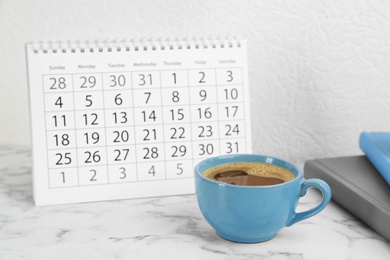 Photo of Composition with calendar and cup of coffee on white marble table
