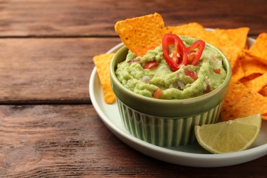 Bowl of delicious guacamole, nachos chips and lime on wooden table, closeup. Space for text