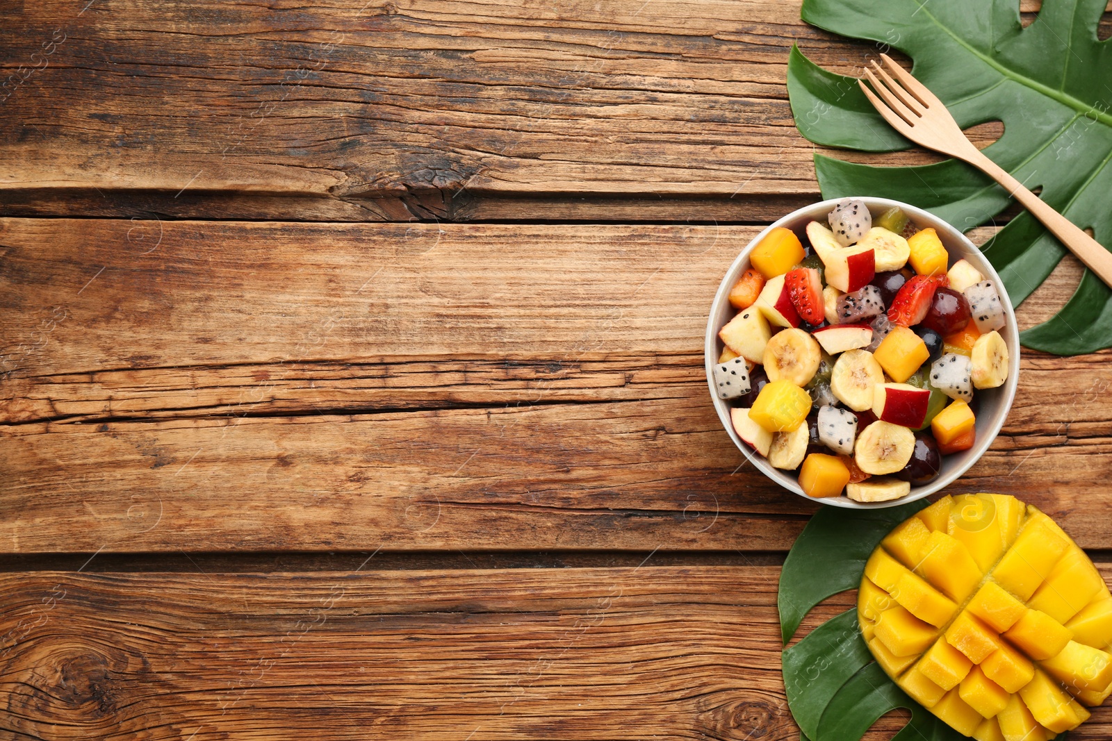 Photo of Delicious exotic fruit salad on wooden table, flat lay. Space for text