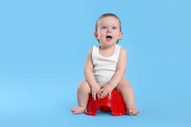 Photo of Little child sitting on baby potty against light blue background. Space for text