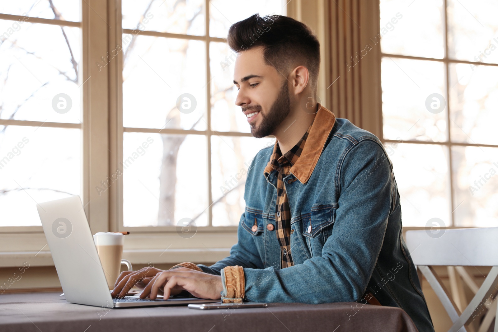 Photo of Young blogger working with laptop at table in cafe