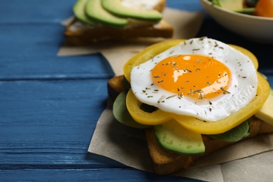 Photo of Tasty toast with fried egg, bell pepper and avocado on blue wooden table, closeup. Space for text