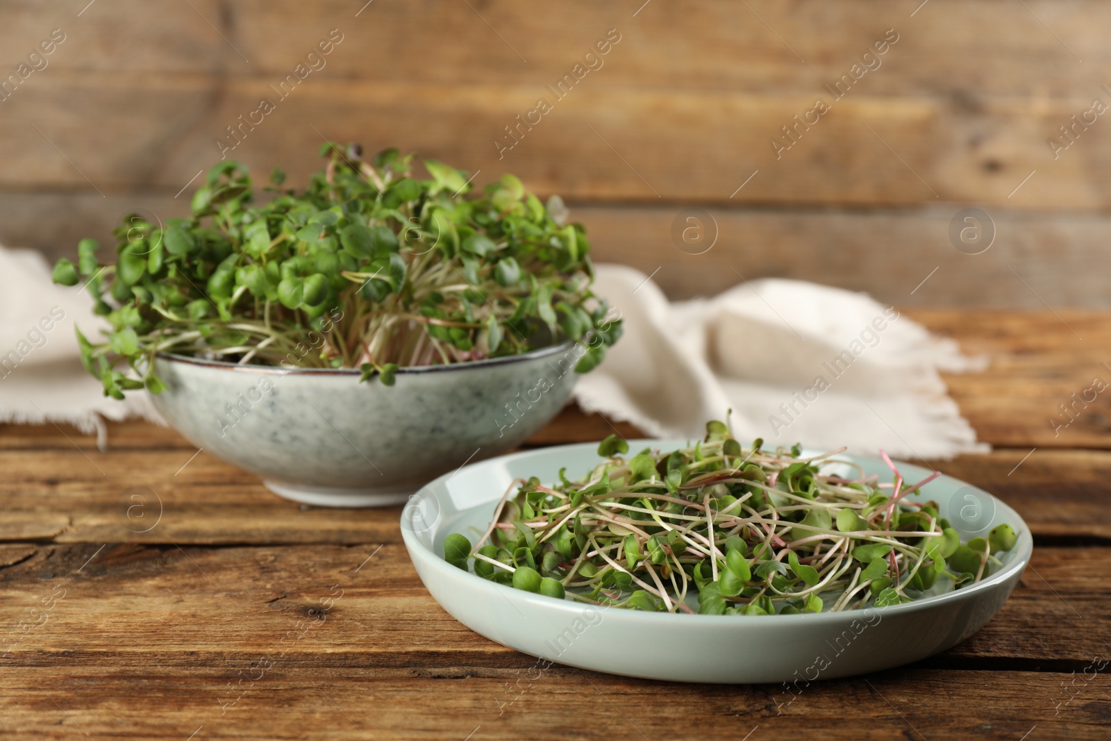 Photo of Plate and bowl with fresh radish microgreens on wooden table