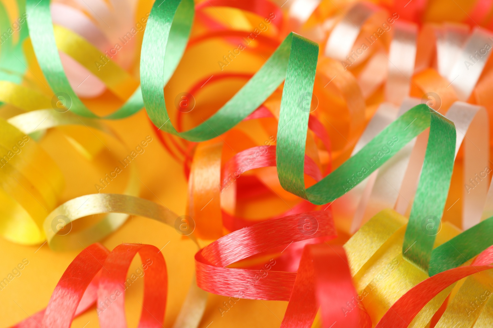 Photo of Colorful serpentine streamers on yellow background, closeup