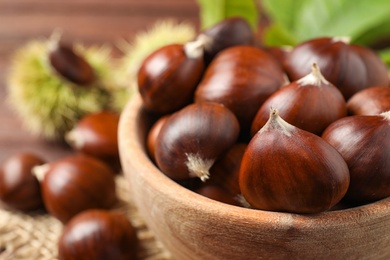 Photo of Fresh sweet edible chestnuts in wooden bowl on table, closeup