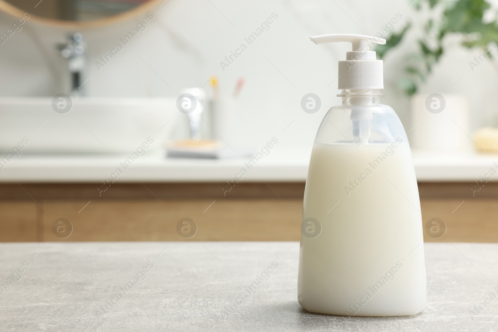 Photo of Dispenser of liquid soap on light grey table in bathroom, space for text