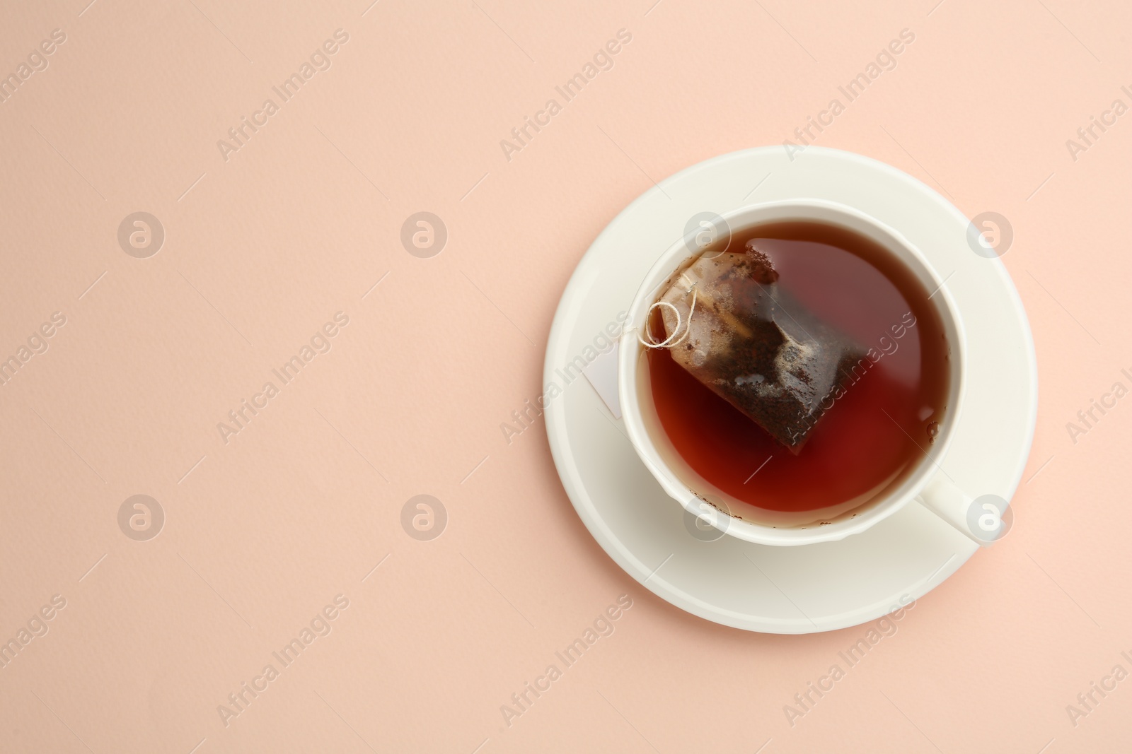 Photo of Tea bag in cup of hot water on pink background, top view. Space for text