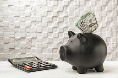 Photo of Black piggy bank with money and calculator on table