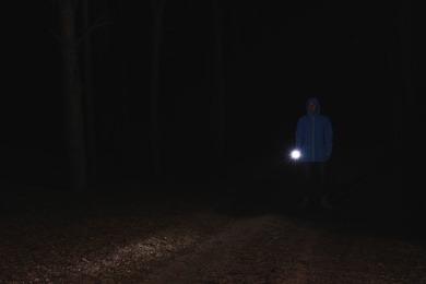 Man with bright flashlight in forest at night