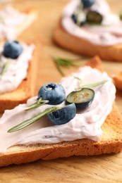Tasty sandwiches with cream cheese, rosemary and berries on wooden tray, closeup