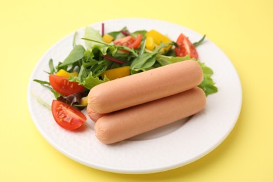 Photo of Delicious boiled sausages with salad on yellow background