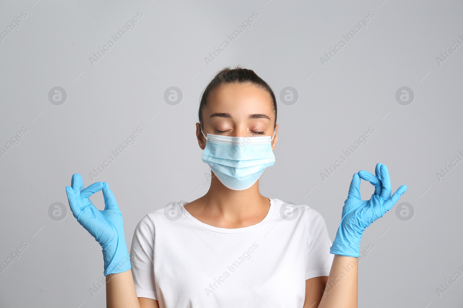 Photo of Woman in protective mask meditating on grey background. Dealing with stress caused by COVID‑19 pandemic