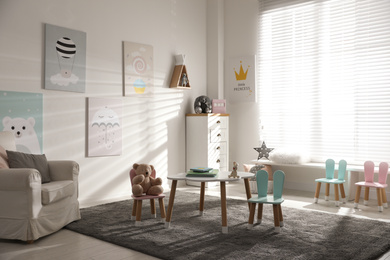 Photo of Small table and chairs with bunny ears in children's room interior