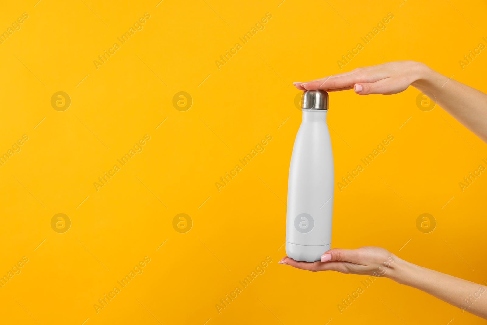 Photo of Woman holding thermos bottle on orange background, closeup. Space for text