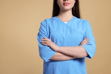 Nurse in medical uniform on light brown background, closeup. Space for text