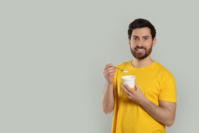 Photo of Handsome man with delicious yogurt and spoon on light grey background. Space for text