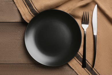 Photo of Clean plate and shiny silver cutlery on wooden table, flat lay