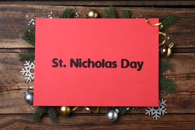 Photo of Red card with text St. Nicholas Day and festive decor on wooden table, flat lay