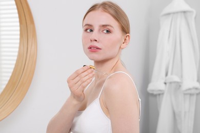 Photo of Woman applying essential oil onto shoulder in bathroom