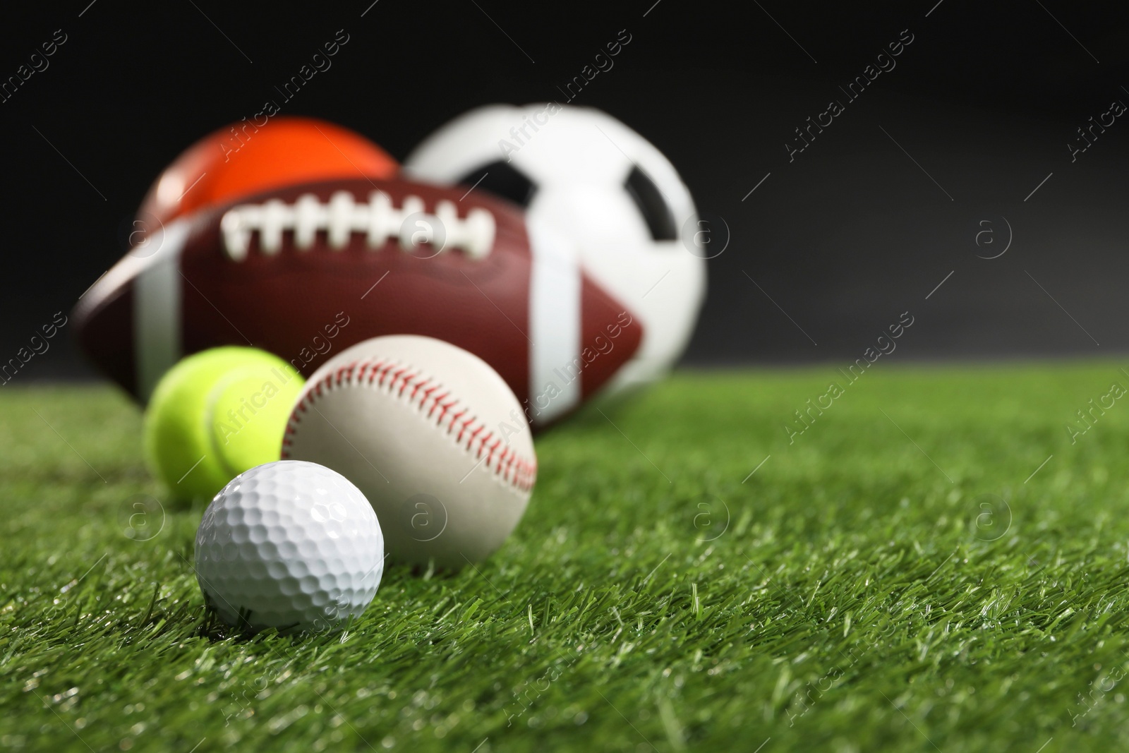 Photo of Many different sports balls on green grass against black background, closeup. Space for text