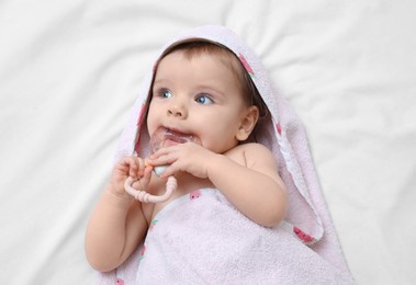 Photo of Cute little baby in hooded towel after bathing nibbling teether on bed, top view