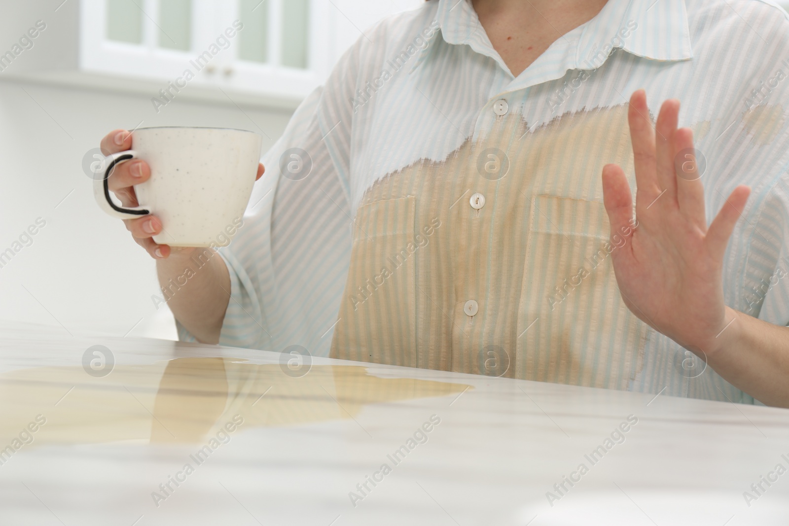 Photo of Woman with spilled coffee over her shirt at marble table indoors, closeup