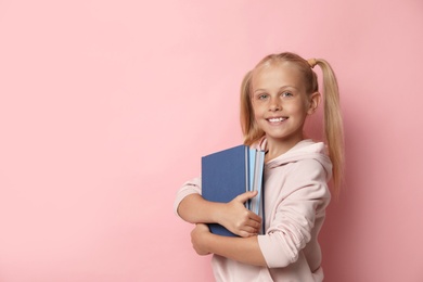 Portrait of cute little girl with books on pink background, space for text. Reading concept