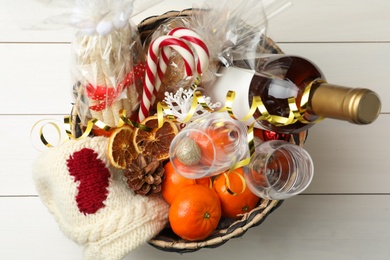 Wicker basket with Christmas gift set on white wooden table, top view