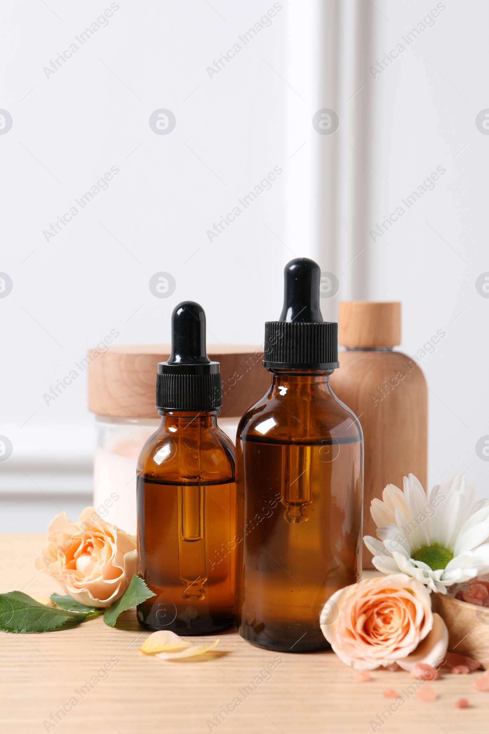 Photo of Bottles of cosmetic serum, beauty products and flowers on wooden table