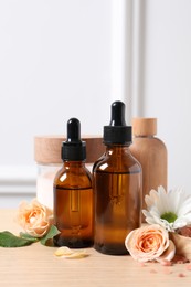 Bottles of cosmetic serum, beauty products and flowers on wooden table