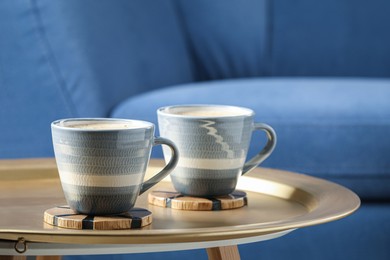 Mugs of coffee with stylish cup coasters on table in room