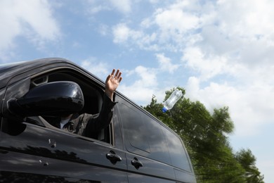 Driver throwing away plastic bottle from car window, low angle view. Garbage on road