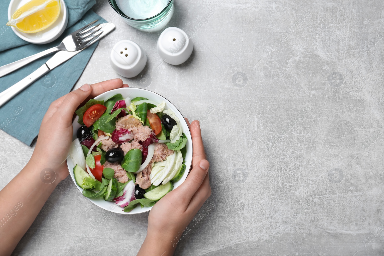 Photo of Woman holding bowl of delicious salad with canned tuna at light grey table, top view. Space for text