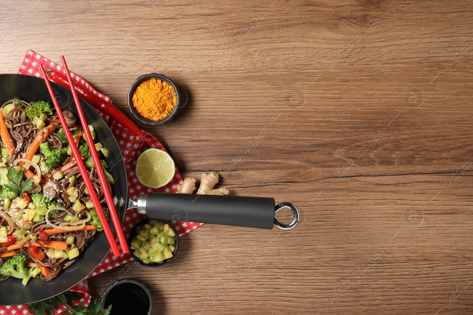 Photo of Stir-fry. Tasty noodles with meat in wok, chopsticks and ingredients on wooden table, flat lay. Space for text