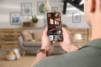 Man using smart home security system on mobile phone indoors, closeup. Device showing different rooms through cameras