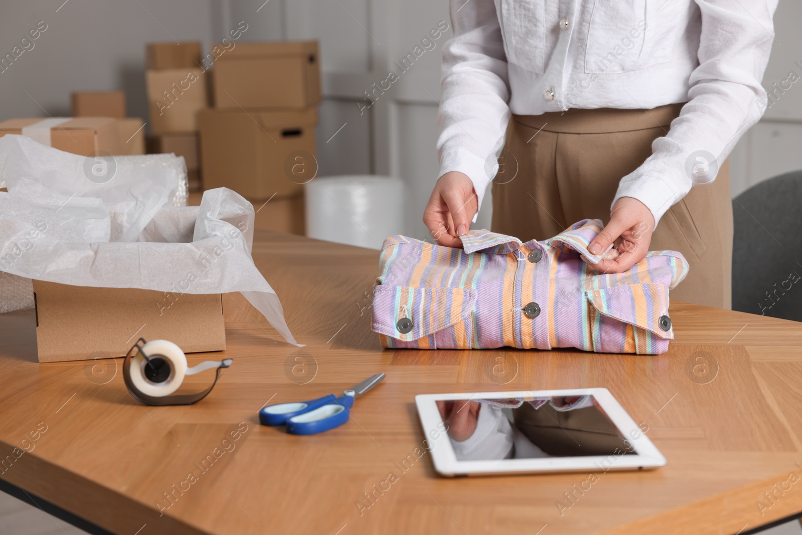 Photo of Seller packing shirt at table in office, closeup. Online store