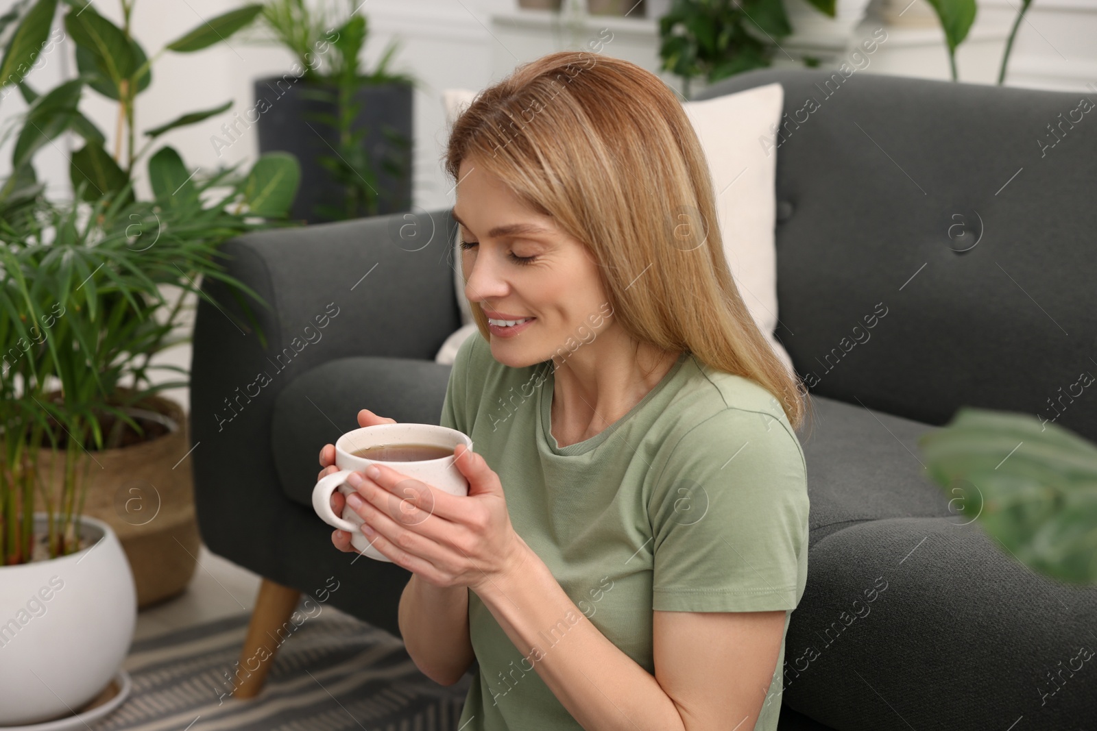 Photo of Woman holding cup of tea in room with beautiful houseplants