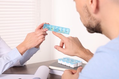 Photo of Doctor holding box of pills and consulting patient at table in clinic, closeup