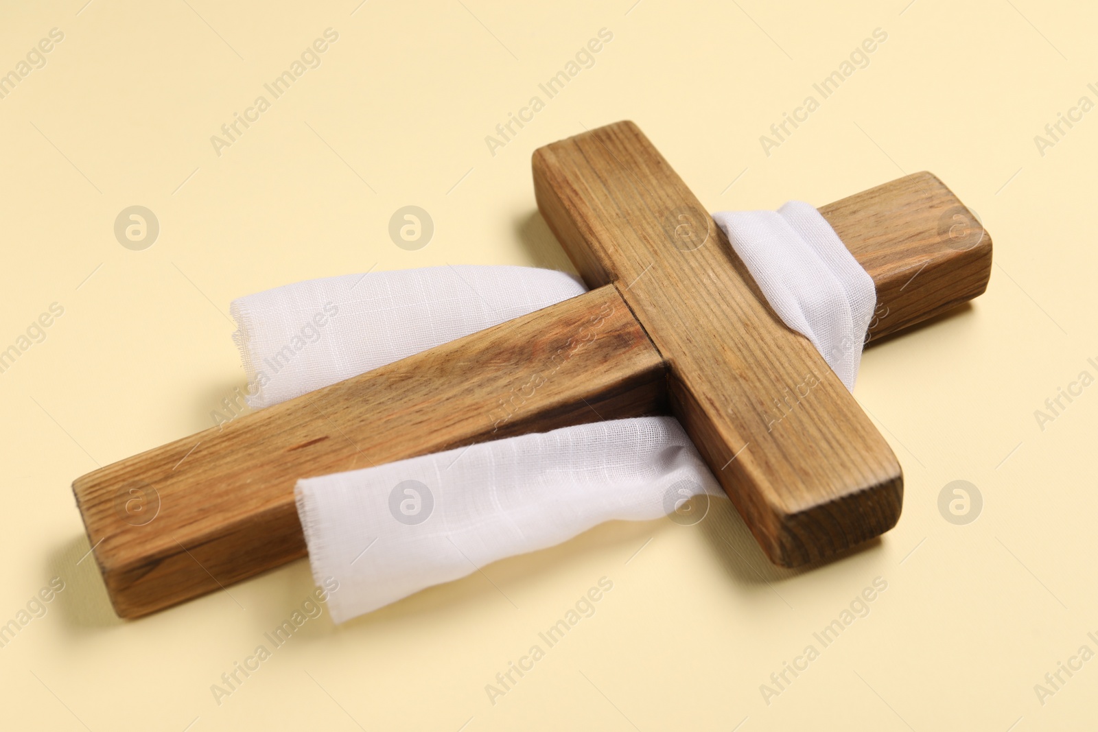 Photo of Wooden cross and white cloth on beige background. Easter attributes