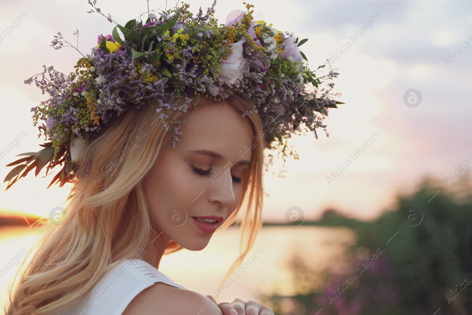 Photo of Young woman wearing wreath made of beautiful flowers outdoors at sunset